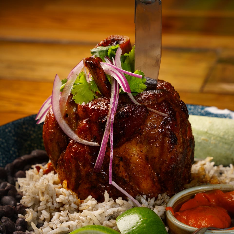 Large glazed meat with a knife, rice, black beans, lime, and red sauce.