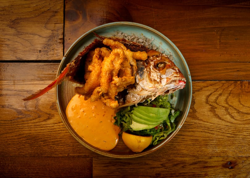 Whole fried fish with crispy skin, battered shrimp, rice, salad, avocado, lemon, and orange sauce.