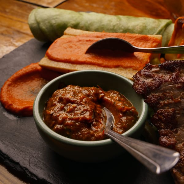 Assortment of grilled meat, green roll, and red-sauced dish with two flavorful dipping sauces.