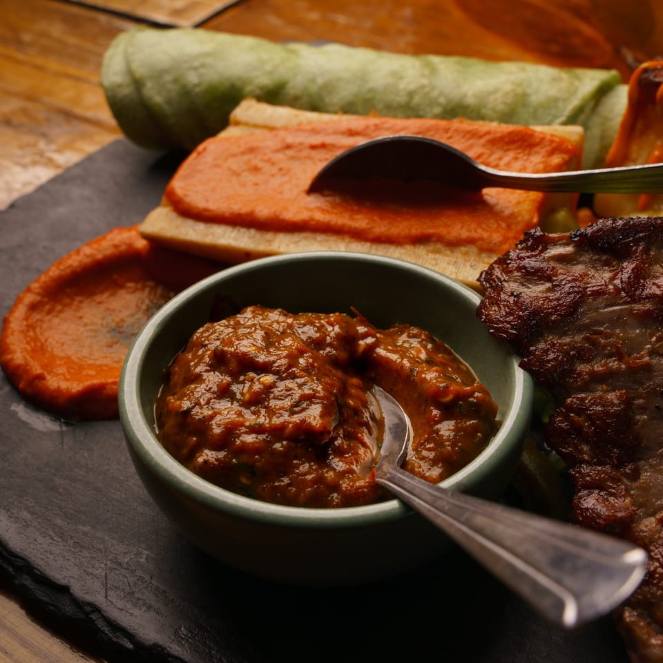 Assortment of grilled meat, green roll, and red-sauced dish with two flavorful dipping sauces.